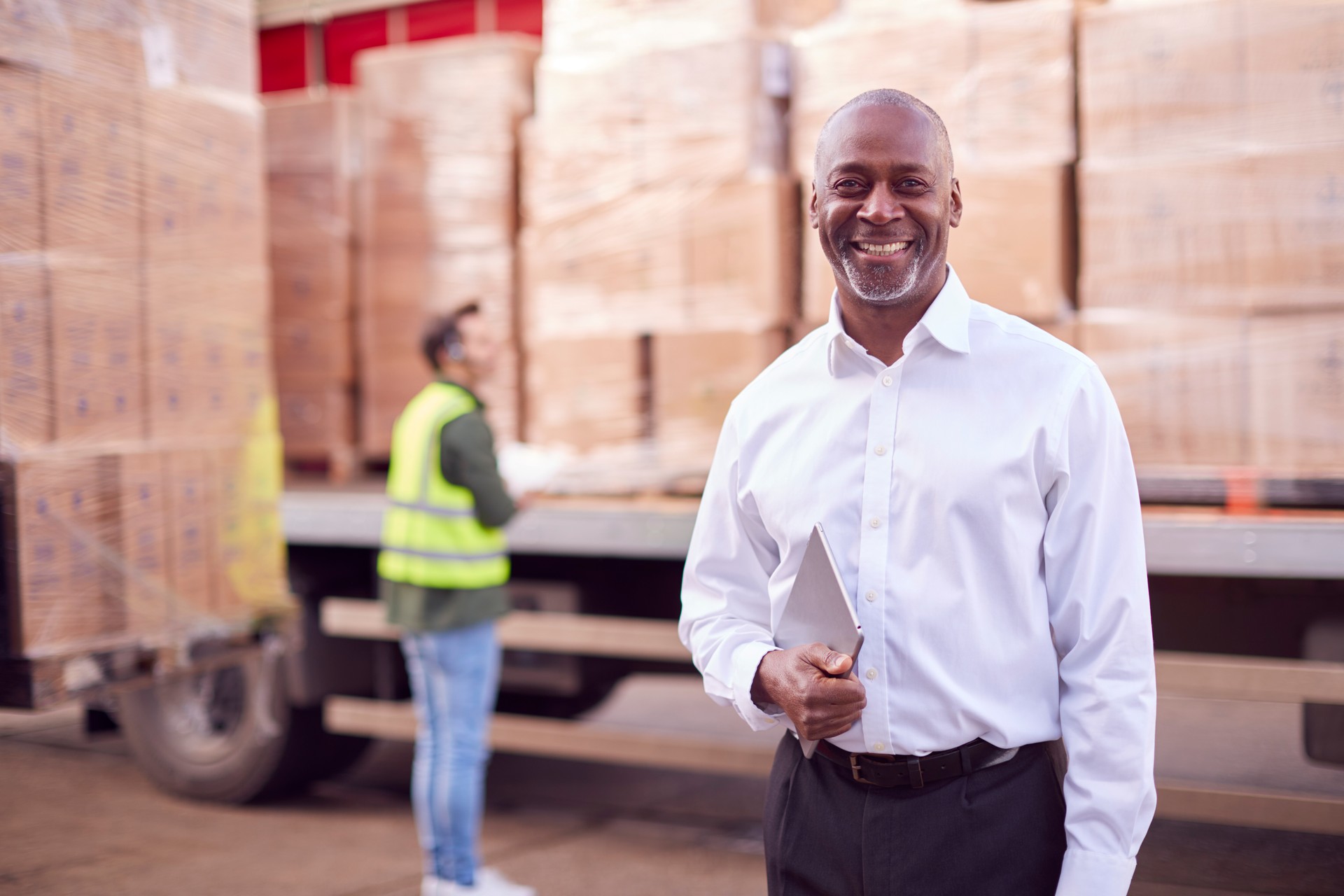 Portrait Of Male Freight Haulage Manager Standing By Truck Being Loaded By Fork Lift