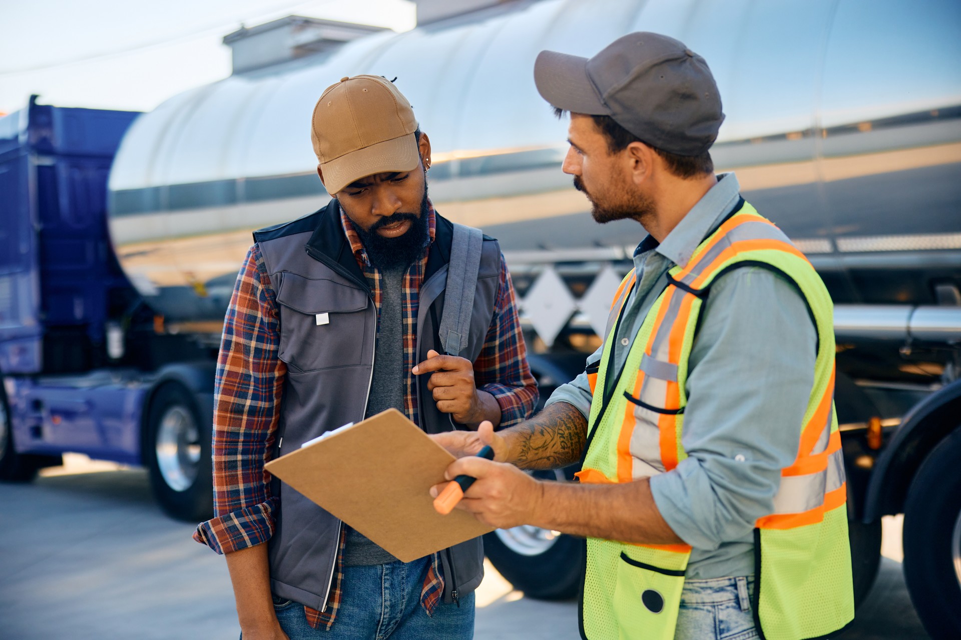 Truck dispatcher and black driver going through shipment list on parking lot.